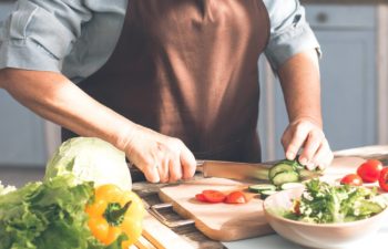 person cutting cucumber on cutting board wearing an apron